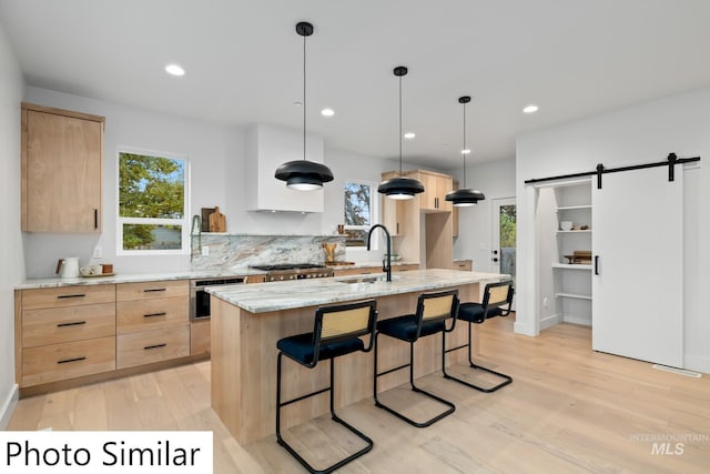 kitchen with light brown cabinets, a barn door, appliances with stainless steel finishes, light wood-style floors, and a sink