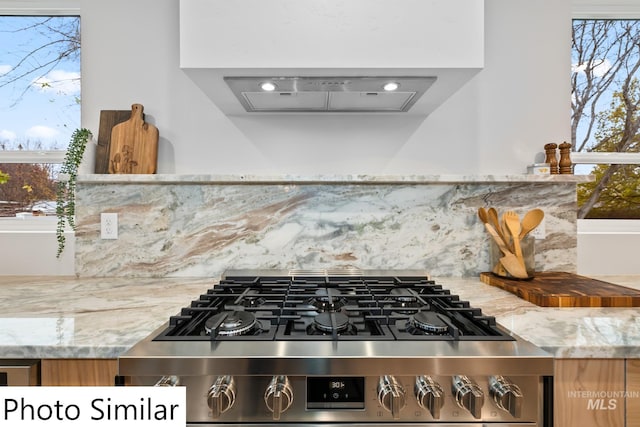 room details featuring decorative backsplash, range hood, stainless steel range with gas cooktop, and light stone countertops