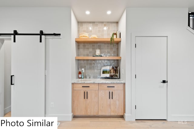 bar with backsplash, recessed lighting, a barn door, light wood finished floors, and baseboards