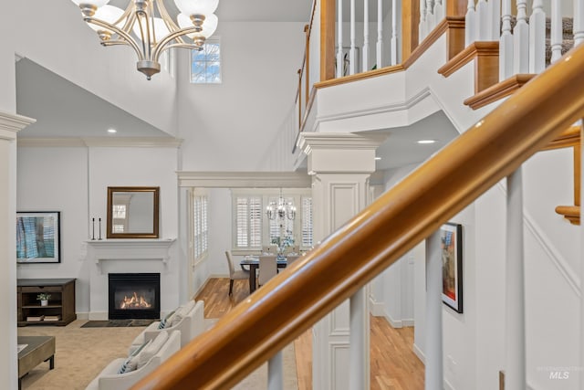 stairway featuring hardwood / wood-style floors, decorative columns, a chandelier, and a high ceiling