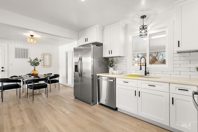 kitchen featuring sink, stainless steel appliances, white cabinets, decorative light fixtures, and light wood-type flooring