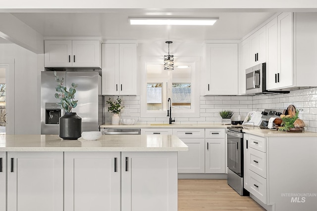 kitchen featuring backsplash, stainless steel appliances, white cabinets, decorative light fixtures, and light wood-type flooring