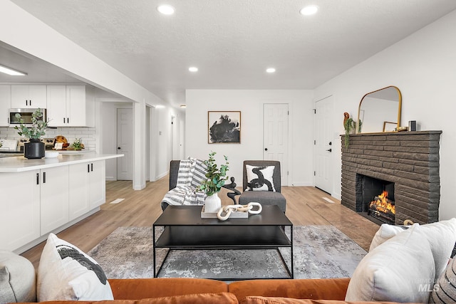 living room with light hardwood / wood-style floors, a brick fireplace, and a textured ceiling