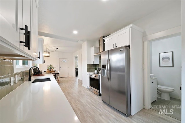 kitchen featuring decorative backsplash, appliances with stainless steel finishes, sink, white cabinets, and light hardwood / wood-style floors