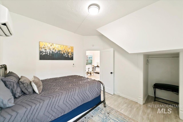 bedroom with wood-type flooring, vaulted ceiling, and a wall unit AC