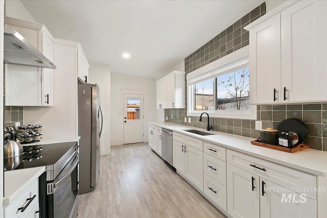 kitchen with white cabinetry, sink, light hardwood / wood-style flooring, decorative backsplash, and appliances with stainless steel finishes