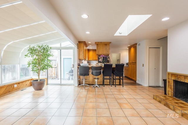 kitchen featuring a skylight, a breakfast bar, a tiled fireplace, brown cabinetry, and a peninsula