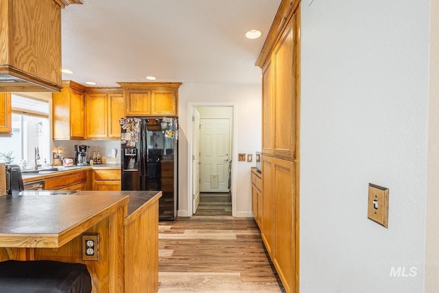 kitchen featuring a peninsula, black fridge with ice dispenser, light wood-style floors, brown cabinetry, and a kitchen bar