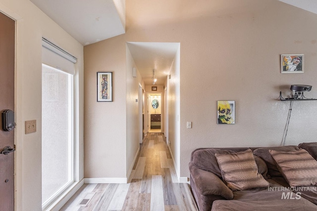 corridor with light wood-style flooring, baseboards, and vaulted ceiling