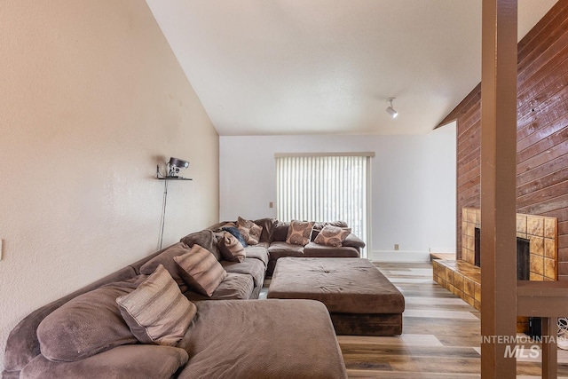 living room with a large fireplace, vaulted ceiling, baseboards, and wood finished floors