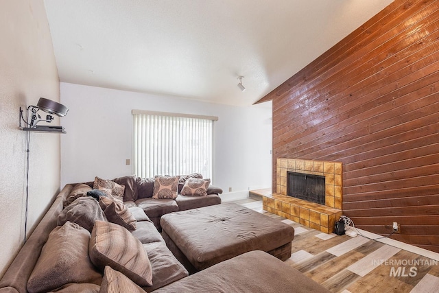 living area with wood walls, vaulted ceiling, wood finished floors, and a tile fireplace