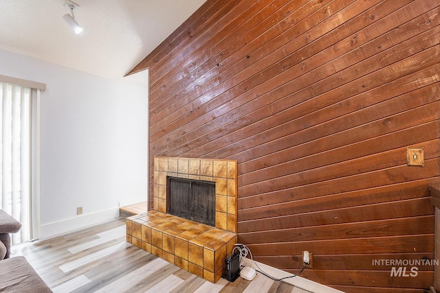 unfurnished living room with lofted ceiling, wood walls, a fireplace, wood finished floors, and baseboards