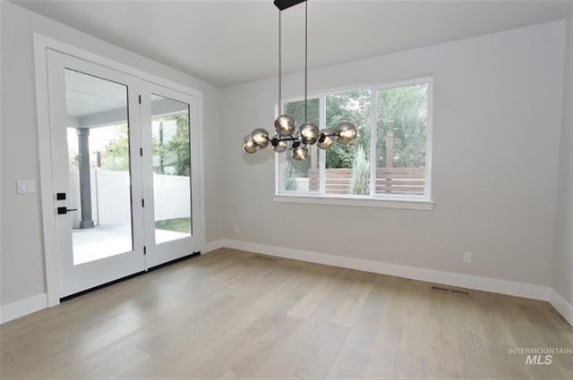 unfurnished dining area featuring french doors, an inviting chandelier, and light wood-type flooring