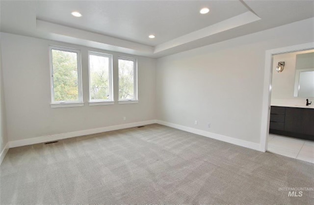 unfurnished bedroom with a raised ceiling, connected bathroom, and light carpet