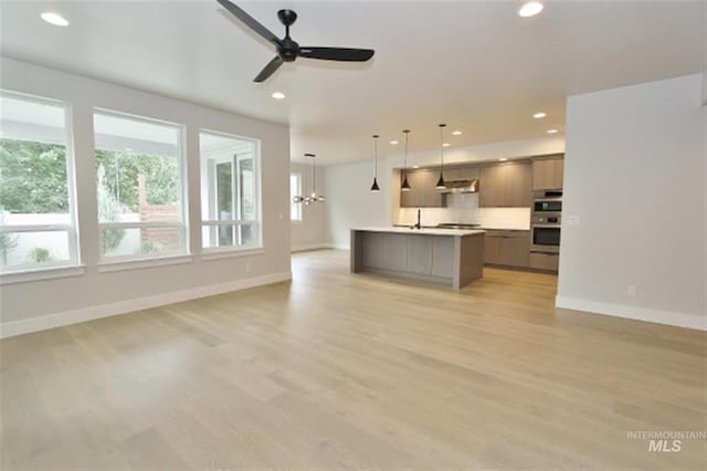 unfurnished living room with light wood-type flooring, sink, and ceiling fan