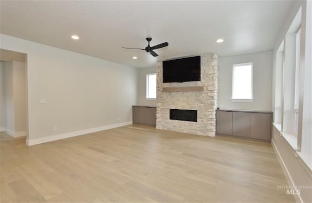 unfurnished living room featuring light hardwood / wood-style flooring, ceiling fan, plenty of natural light, and a stone fireplace