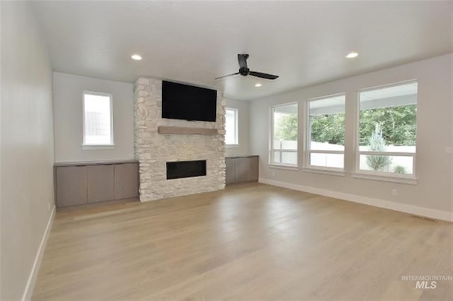 unfurnished living room with a stone fireplace, light hardwood / wood-style flooring, ceiling fan, and plenty of natural light