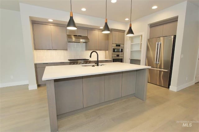 kitchen with decorative light fixtures, appliances with stainless steel finishes, light wood-type flooring, and sink