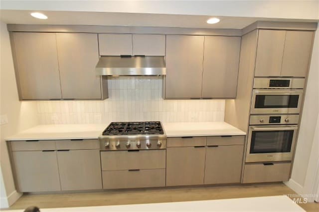 kitchen featuring backsplash, gray cabinets, stainless steel appliances, and light wood-type flooring