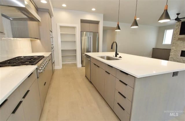 kitchen with an island with sink, sink, decorative light fixtures, wall chimney exhaust hood, and light wood-type flooring