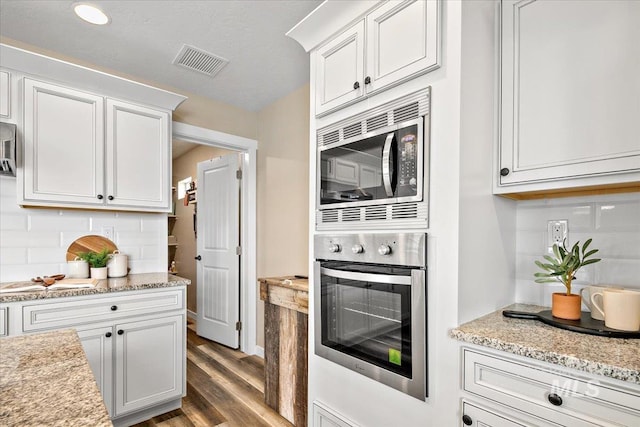 8618 Latimore Ln, Middleton, ID 83644 - kitchen with appliances with stainless steel finishes, wood finished floors, tasteful backsplash, white cabinets, and light stone counters