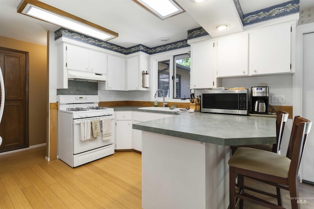 1719 S Gekeler Ln, Boise, ID 83706 - kitchen featuring white range with gas stovetop, stainless steel microwave, under cabinet range hood, a sink, and a peninsula