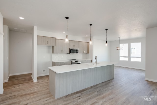 kitchen featuring an island with sink, stainless steel appliances, light brown cabinetry, and light hardwood / wood-style flooring