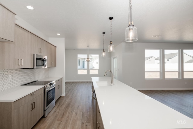 kitchen with sink, hanging light fixtures, light hardwood / wood-style flooring, light brown cabinetry, and stainless steel appliances