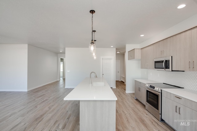 kitchen featuring sink, decorative light fixtures, a kitchen island with sink, appliances with stainless steel finishes, and light wood-type flooring