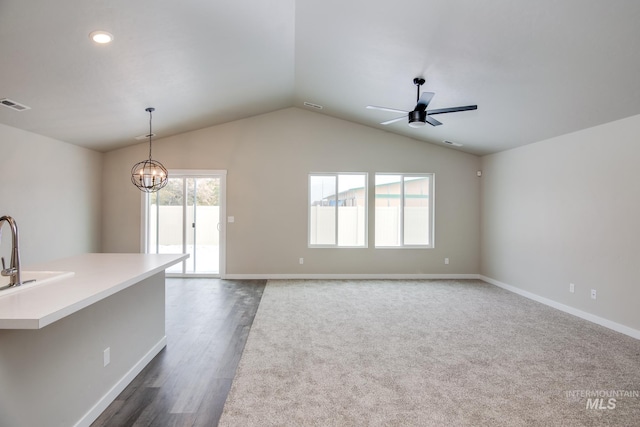 spare room with a healthy amount of sunlight, vaulted ceiling, ceiling fan with notable chandelier, and dark hardwood / wood-style flooring