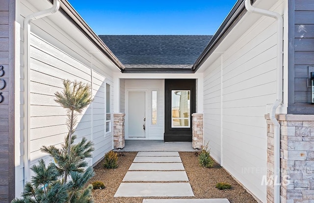 view of exterior entry featuring roof with shingles