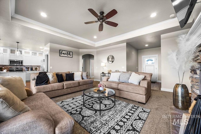 carpeted living room featuring a raised ceiling, ornamental molding, and ceiling fan