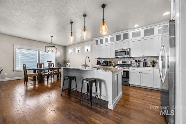 kitchen with white cabinetry, hanging light fixtures, a center island with sink, stainless steel appliances, and backsplash