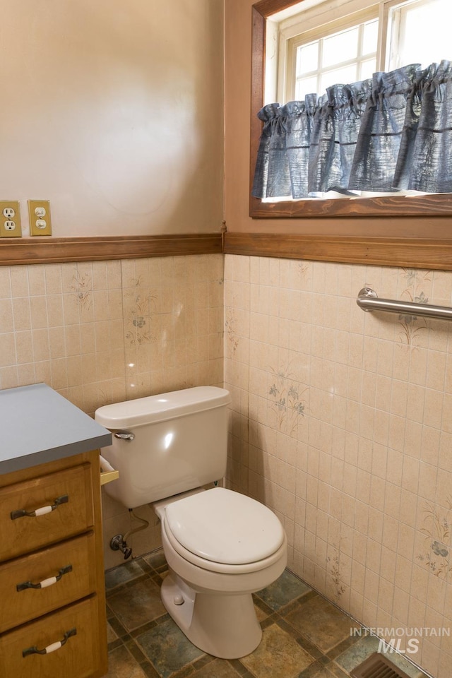 286 SW 3rd Ave, Ontario, OR 97914 - half bathroom with tile walls, vanity, toilet, a wainscoted wall, and stone finish floors