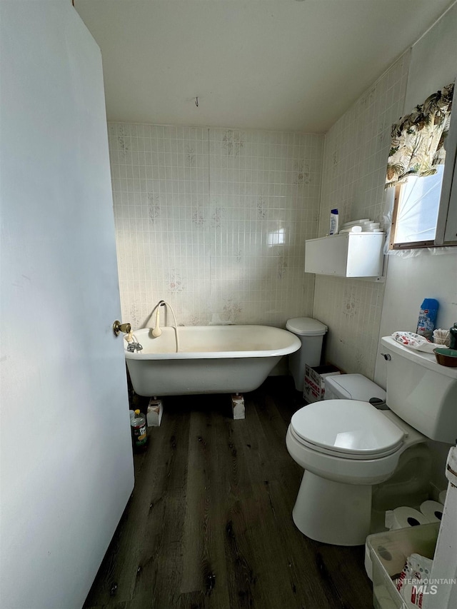 bathroom with hardwood / wood-style floors, a tub, tile walls, and toilet