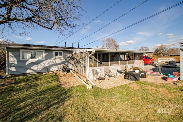 rear view of property featuring a gate, a lawn, a sunroom, and fence