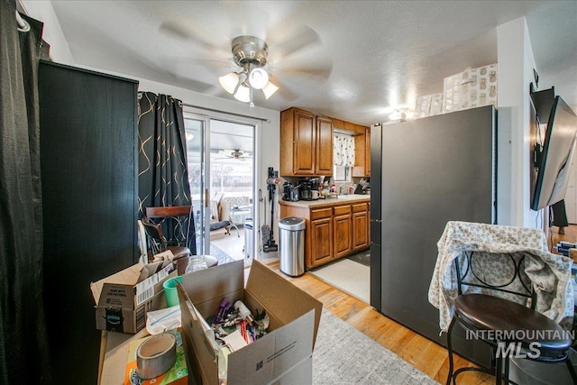 kitchen with light countertops, brown cabinets, light wood-style flooring, freestanding refrigerator, and a ceiling fan