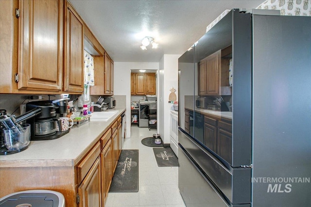 kitchen with light floors, light countertops, freestanding refrigerator, independent washer and dryer, and a sink