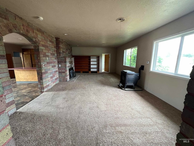 living room with carpet floors, a textured ceiling, a brick fireplace, and a wood stove