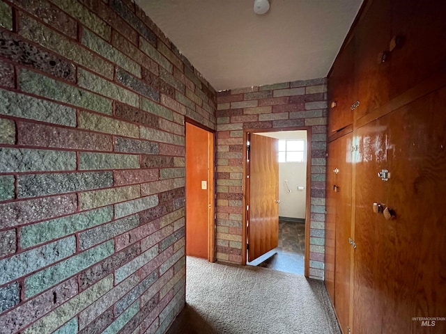 hall with dark colored carpet and brick wall