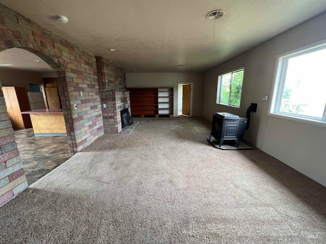 unfurnished living room featuring a brick fireplace, a textured ceiling, carpet, and a wood stove