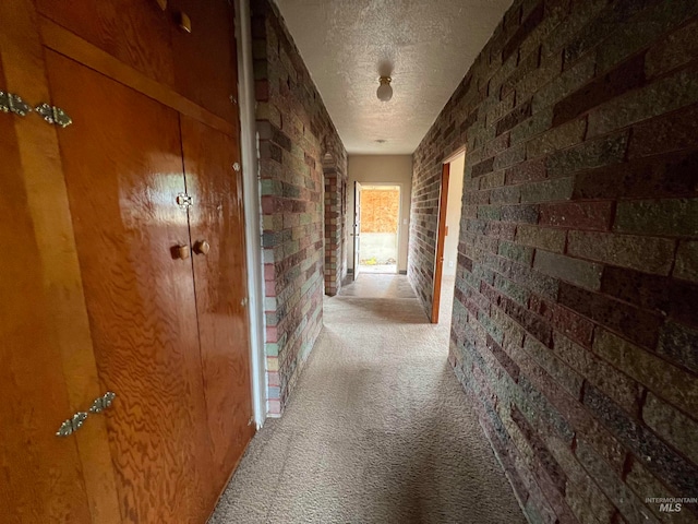 corridor with carpet floors, a textured ceiling, and brick wall