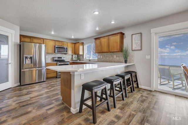 kitchen with dark hardwood / wood-style flooring, appliances with stainless steel finishes, a kitchen breakfast bar, and kitchen peninsula