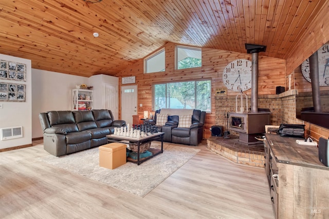 living room featuring visible vents, wood finished floors, wooden walls, wooden ceiling, and a wood stove