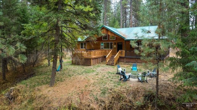 exterior space featuring a wooden deck, stairway, a wooded view, and an outdoor fire pit