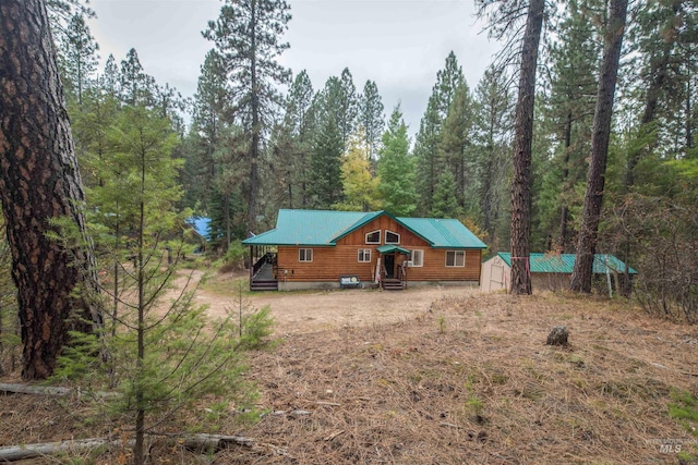 view of front of property featuring a wooded view, metal roof, an outdoor structure, and dirt driveway