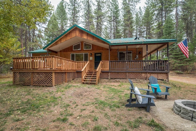 rear view of property with a wooden deck, a fire pit, metal roof, and faux log siding