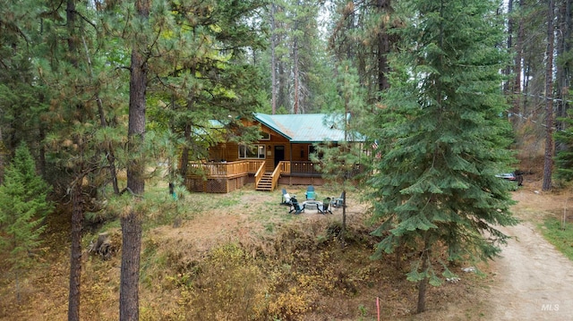 view of yard with a deck, a wooded view, driveway, and an outdoor fire pit