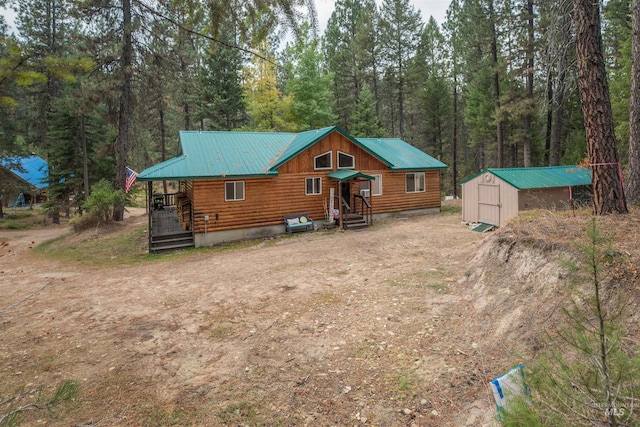 view of front facade with a view of trees, dirt driveway, a storage shed, an outdoor structure, and metal roof