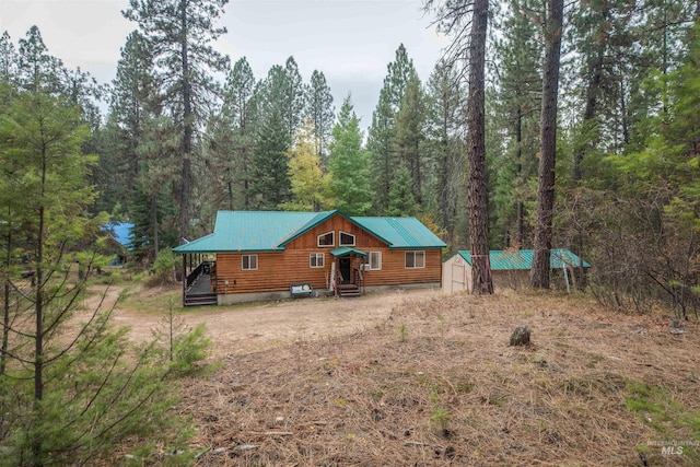 view of front of home with metal roof, a storage shed, an outdoor structure, and a wooded view